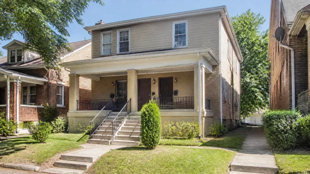 A two-storey multifamily building with a shared front porch and steps up from the sidewalk.