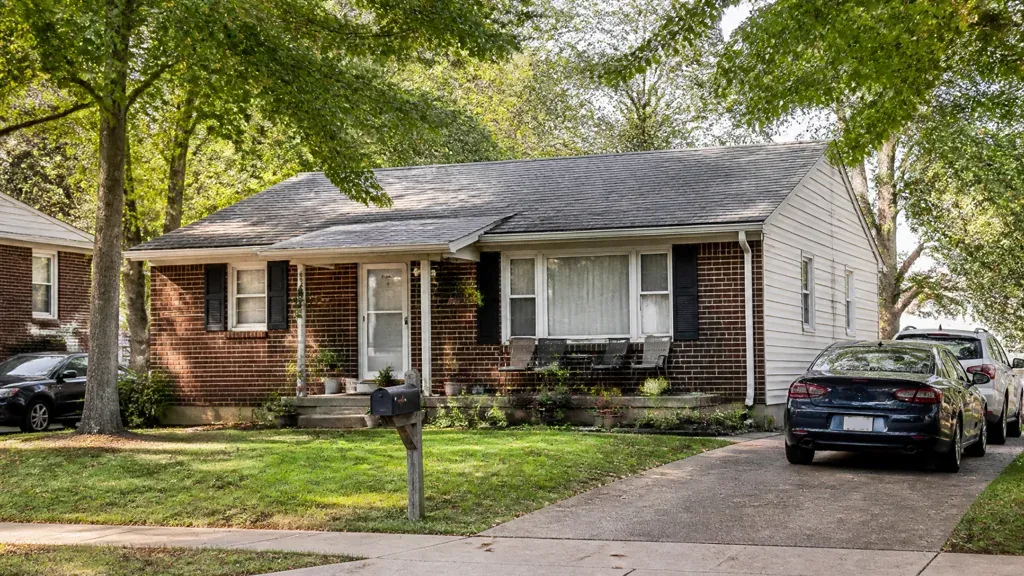 A brick ranch house seen from the street with cars parked along the kerb.
