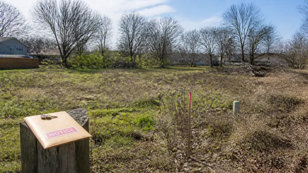 A bare winter lot with a notice envelope resting on a tree stump in the foreground.